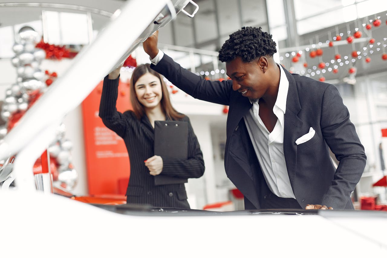 about-img Positive smiling diverse stylish man and female dealer checking under car motor hood and smiling while choosing new car in car showroom